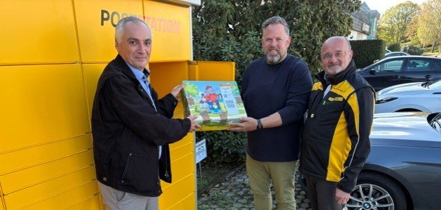 Eröffnung der Poststation Gusterath, 3 Männer lächeln in die Kamera und halten ein Paket.