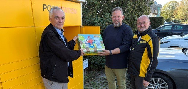 Eröffnung der Poststation Gusterath, 3 Männer lächeln in die Kamera und halten ein Paket.