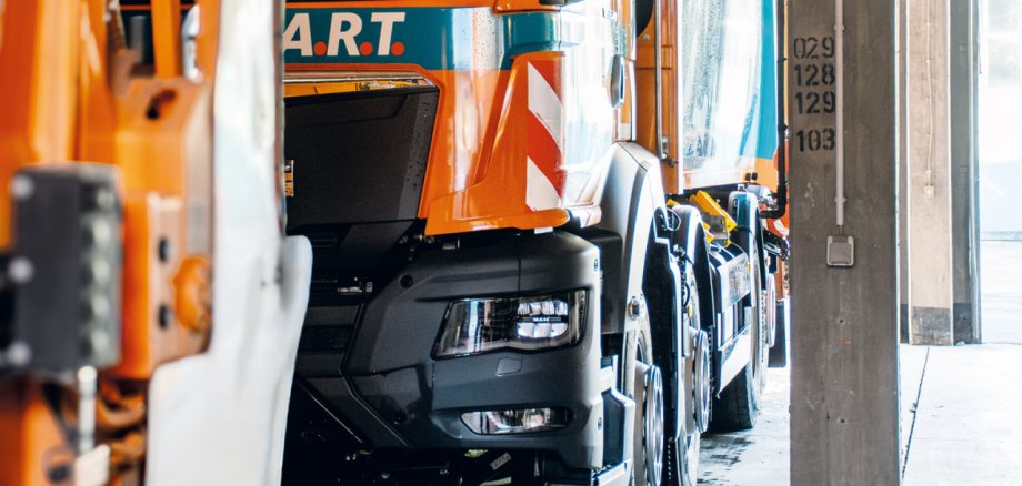 Müllauto in den Farben orange und grün, welches in einer großen Garage geparkt ist.