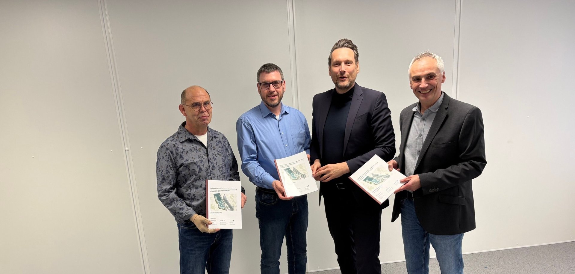 4 lächelnde männliche Personen schauen in die Kamera und präsentieren Pläne