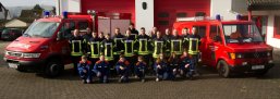 Gruppenfoto einer Feuerwehrmannschaft in Schutzkleidung vor einem Einsatzfahrzeug in einer Fahrzeughalle.