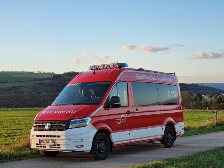Roter Mannschaftstransportwagen der Feuerwehr fährt auf einer Straße durch offene Landschaft.