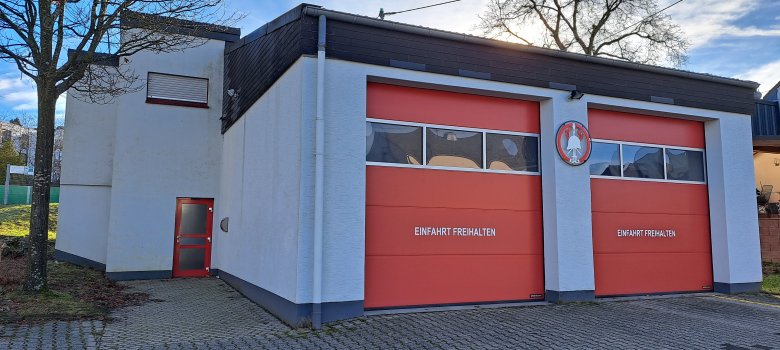Modernes Feuerwehrgerätehaus mit zwei großen roten Hallentoren und Vorplatz.
